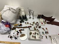 Wide view of holiday village figurines, miniature train set, trees, cotton batting and boxed accessories spread out on white surface.