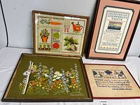 Four framed needlework and cross-stitch art pieces arranged against a white wall showing details of design and framing.