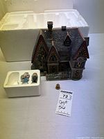 Porcelain Department 56 Dickens Village house from the Great Expectations series with two character figurines in original styrofoam packaging, placed on a flat surface with auction tag visible.