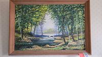 Front view of framed landscape painting showing woodland stream scene with trees, rocks, and flowing water.