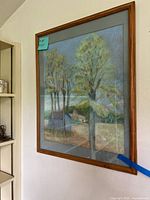 Framed landscape painting with wood frame showing trees and buildings, with light blue background.