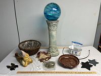 Photo showing all items in the lot including garden orb on pedestal, gnome figurine, hanging basket, ceramic planter, stained glass butterfly, fabric doll, dried moss, metal brackets, and ceramic dish.
