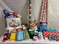 Various gift wrapping and party supplies arranged including gift bags, tissue papers, multiple rolls of wrapping paper, ribbons, gift tags, bows, and a party hat.