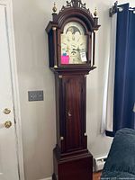 Full view of tall-case grandfather clock in mahogany finish against wall