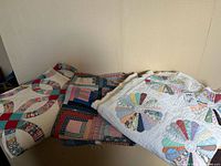 Three folded quilts displayed on a flat surface against a wall