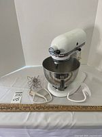 White KitchenAid Ultra Power electric stand mixer with stainless steel bowl and three attachments on white surface.