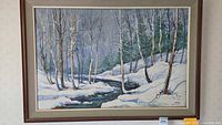 Framed oil on canvas winter landscape painting depicting trees and a stream with snow. Signed by artist in lower right corner.