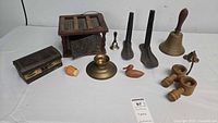 Lot of assorted vintage wood and metal collectibles on white table including hand-painted wooden box, brass bell, wooden shoe forms, wooden bird, grater box, and other small items.