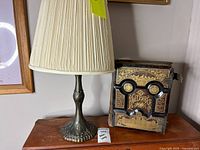 Lamp with fabric shade and ornate Holy Bible on wooden surface, photo includes detailed view of Bible's cover and lamp base.