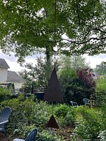 Outdoor hanging metal wind chime with large triangular main plate and smaller star-shaped plate, hangs from a chain in a garden setting.