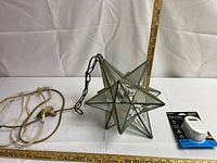 Photo showing the Moravian star-shaped light fixture with electrical cord and hanging chain beside measuring rulers showing size