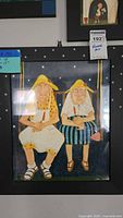 Framed watercolor folk art painting showing two elderly women sitting on a swing at night, wearing summer hats and casual clothing.