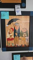 Frontal view of a framed watercolor painting showing three elderly figures sitting on a bench under a black umbrella in the rain, each wearing glasses and distinctive clothes. Dimensions visible on sticky note: Height 17 inches, Width 14 inches, Depth unknown.