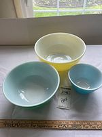 Three Pyrex bowls arranged in descending order of size against window light showing teal, green, and yellow colors with white interiors.