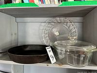 Cast iron skillet, Pyrex casserole dish with lid, and Pyrex pie plate on a shelf.