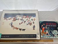 Framed print of Art Expo New York 1984 by Rie Muñoz with hardcover book 'Portrait of Alaska' placed on a table.