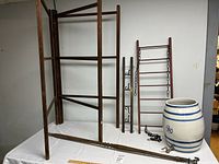 Wooden rack, two wooden ladders, ceramic barrel with spigot, and metal chain displayed on a white surface against a wall.