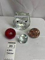 Front view of all four glass pieces on white surface; includes clear glass owl figurine and three round paperweights in red, multicolor, and clear glass.