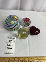 Set of four decorative glass paperweights placed on white surface, showing size scale with ruler and a MaxSold tag.