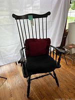 Black wooden Windsor arm chair showing spindle back, turned legs, curved armrests, on hardwood floor against white backdrop.