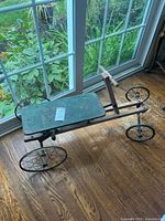 Photo of the full vintage pedal car showing wooden seat with faded green paint and metal spoked wheels.