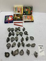 Photo showing 20 metal leaf and floral shaped candle holders arranged in rows on white surface with two loose red taper candles.