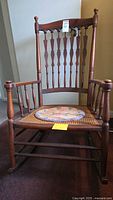 Frontal view of the vintage wooden rocking chair showing woven cane seat and turned spindle backrest with floral round cushion.