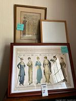View showing three framed prints leaning against a wall including manuscript text and large rectangular fashion illustration print with six women.