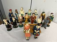 Front angled overview of all 18 painted resin elderly caricature figurines in various poses and outfits on white cloth background.