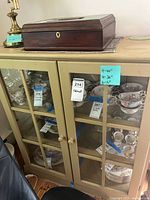 Front view of beige/tan wooden shelving cabinet with glass paneled doors showing interior shelving with various dishes (not included). Dimensions noted on sticky note: Height 40 in, Width 36 in, Depth 15 in.