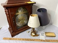 Photo of lot showing wood mantel clock, two table lamps, gold-tone clutch wallet, ruler for scale