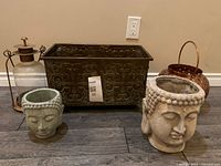 Group view showing both ceramic Buddha head planters, rectangular metal planter, copper-tone bucket planter and glass lantern