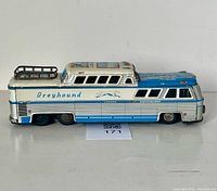 Left side view of tin Greyhound bus showing roof rack and graphics