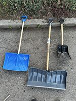 Three snow shovels laid out on ground showing blade shapes, colors and handles