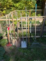 Group shot of all eight long-handled tools leaning against garden bed