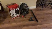 Vacuum, hose, wand, floor nozzle and box displayed on floor