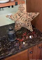 Large woven star, black lantern and three metal star ornaments displayed on countertop
