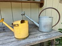 Yellow and galvanized watering cans on wooden bench