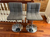 Front view of both grey swivel bar stools showing seats, backs and chrome bases
