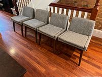 Four grey upholstered dining chairs in a row on wood floor