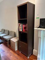 Front view of tall dark brown shelving unit showing three open shelves and cabinet door