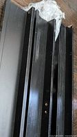Three black IKEA picture ledges stacked, showing mounting holes and overall condition