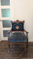 Front view of carved wood armchair showing needlepoint back panel and velvet seat