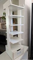 Full view of white vertical rack, five shelves, bottom drawer closed