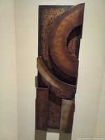 Abstract rectangular metal wall art with layered curved and straight panels in earth tones.