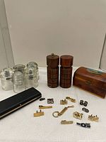 Photo showing five clear glass hydro insulators, two wooden salt and pepper mills, a wooden jewelry box with colorful painted design, and assorted men's tie clips and cuff links spread out on a table.