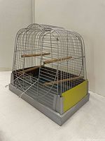 Side view of the bird cage showing the wire construction, plastic base with yellow food holders, wooden perches inside, and a carry handle on top.