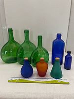 Photo showing all 8 coloured bottles including 3 large green bottles, 2 blue bottles, and 3 tri-coloured small decanters with cork lids