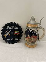 Decorative metal saw sign with 'PaPa's fix it shop' text and beer stein showing full body side view