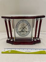 Front view of the Forestville mantle clock showing wooden frame with glass panels and visible internal gears, ruler placed below for size reference.